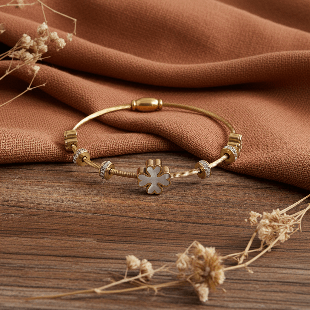 3 leaf charm bracelet with 18k gold plating  on brown fabric and brown top.