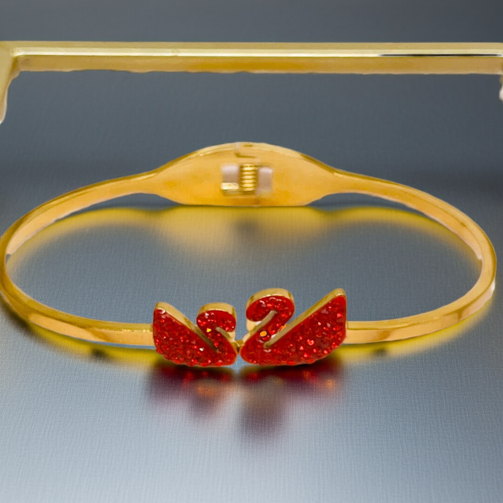 Gold bracelet with red heart-shaped swan on a reflective surface