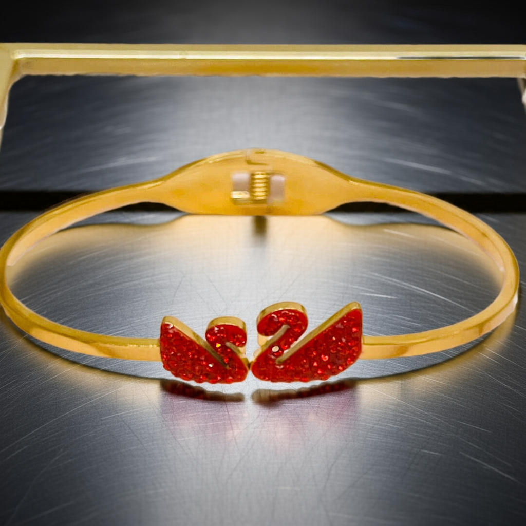 Gold bracelet with red swan on a metallic surface