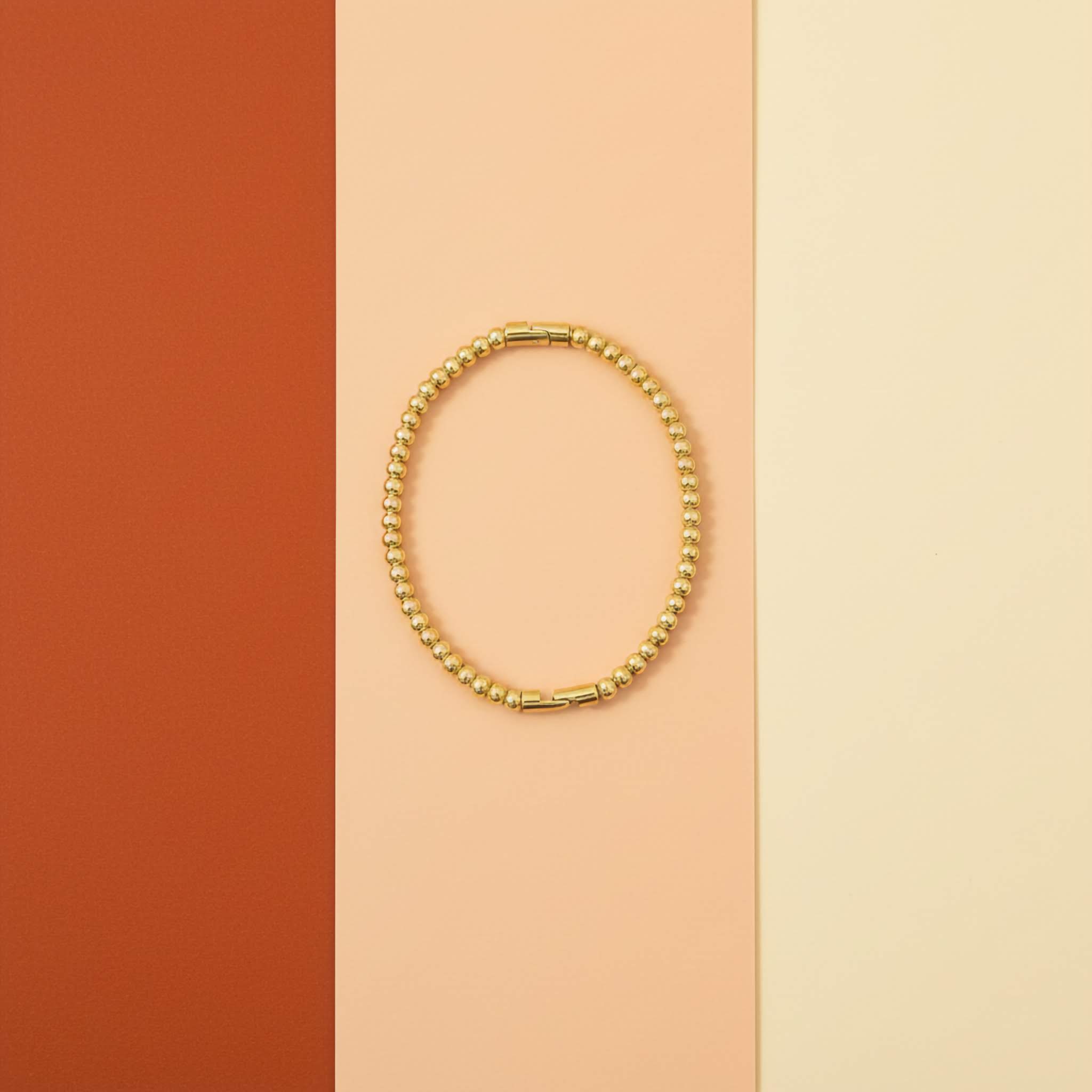 18k Gold plated beaded bracelet on a two-tone orange and beige background