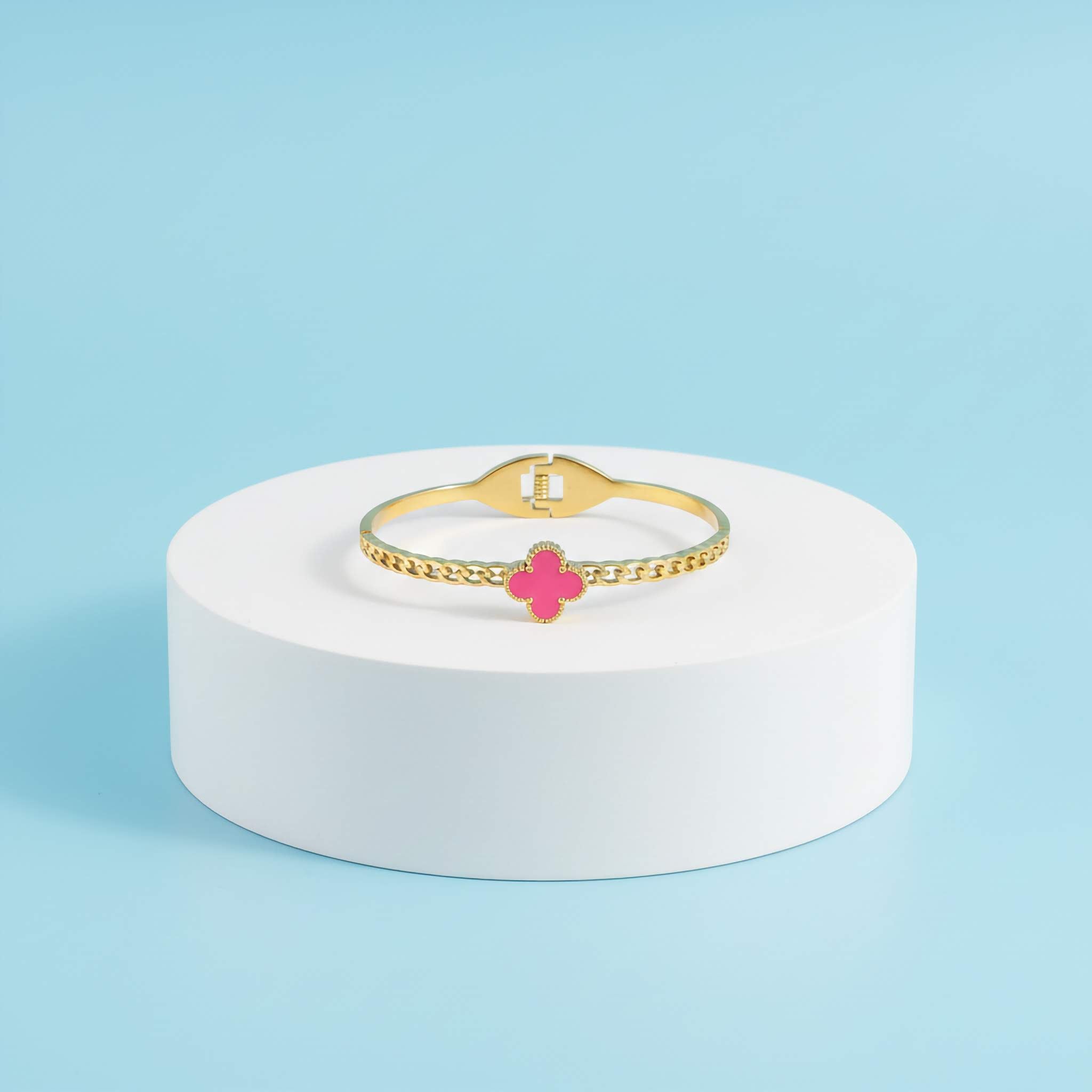 18k Gold plated bracelet with a pink clover charm on a white stand against a light blue background