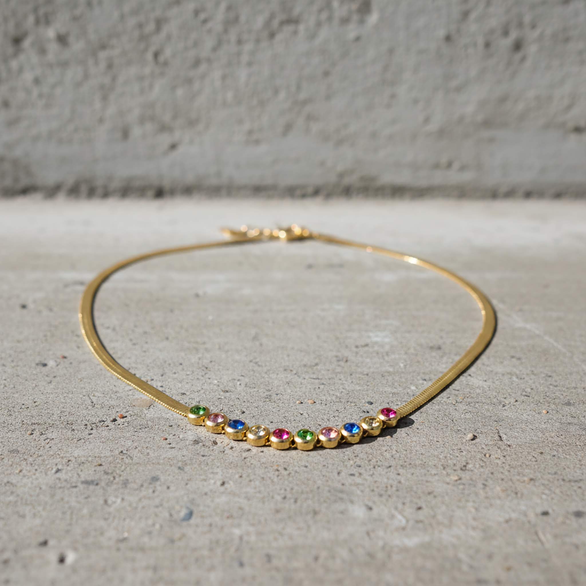 Gold plated necklace with colorful zirconia diamonds on a concrete surface