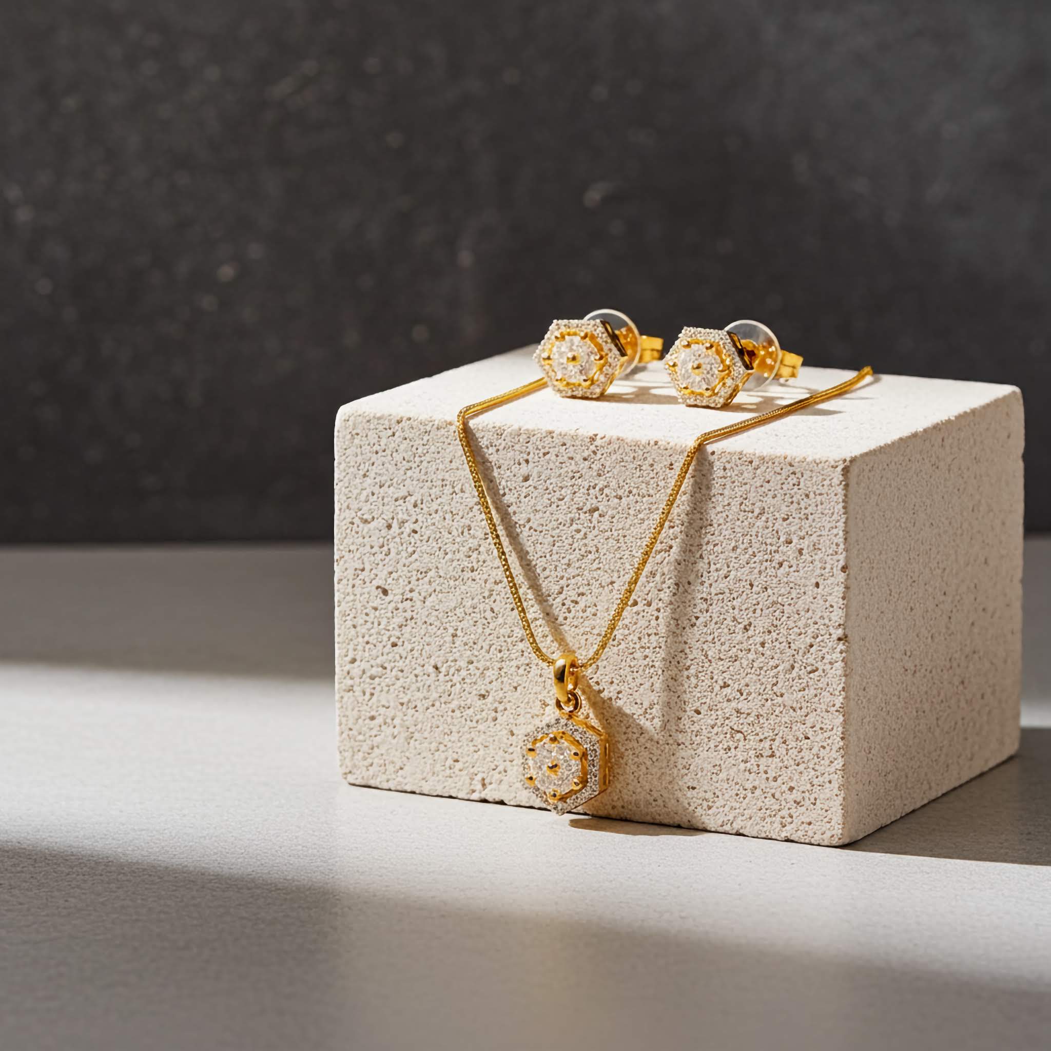 Hexagon shape zirconia diamond jewelry set of 18k Gold plated necklace and earrings on a textured cube with a dark background