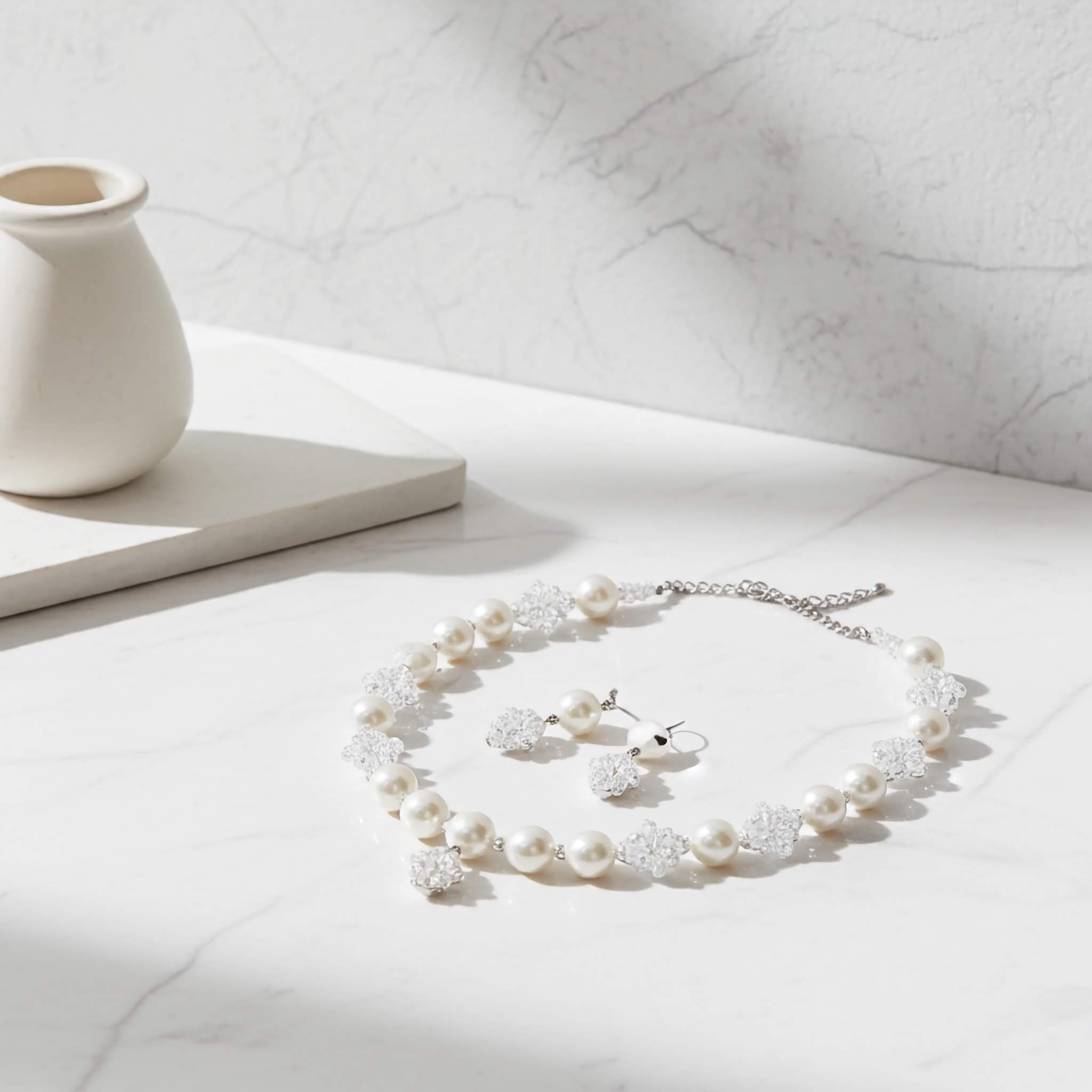 A White Pearl necklace and earrings set on a light surface with a marble wall background