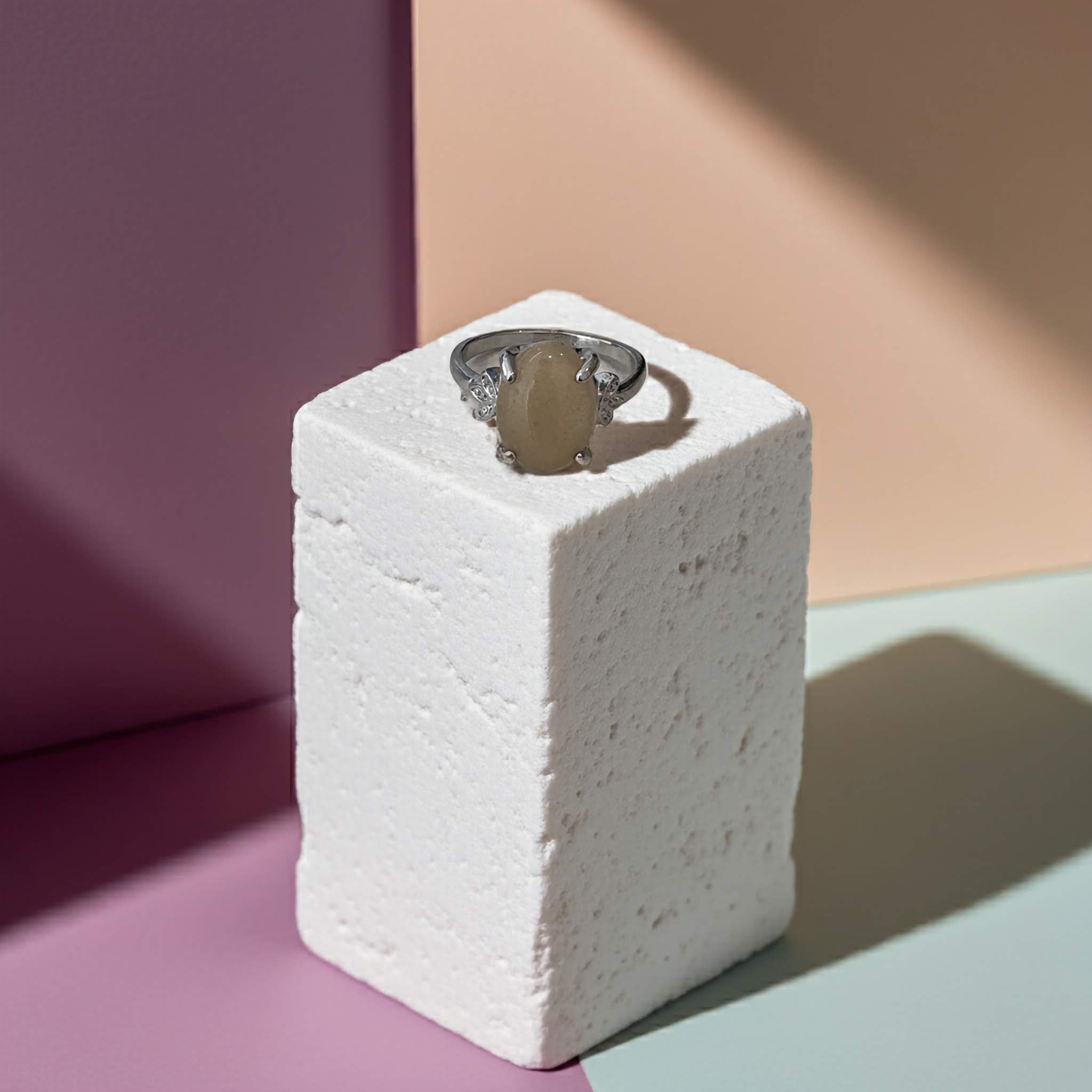 Beige gemstone on a Silver clasp ring on a textured white block against a colourful background