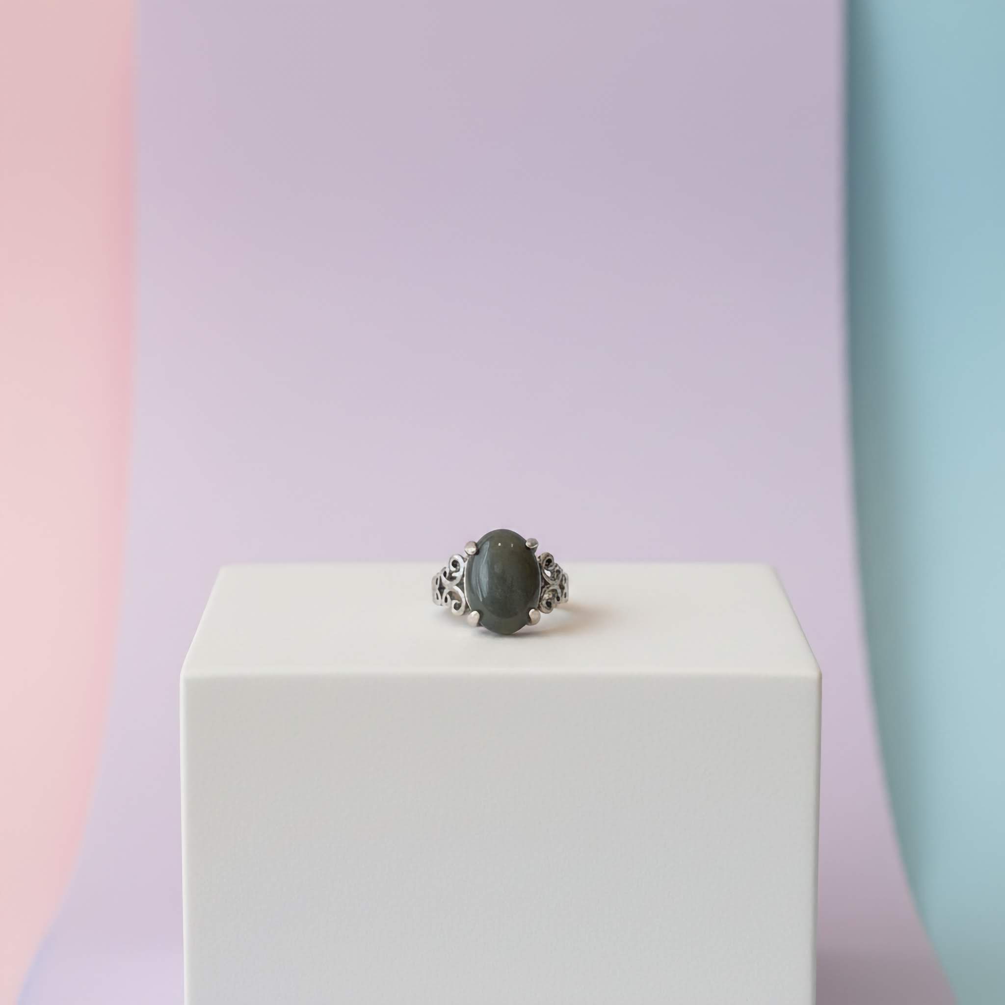 Ring with a dark stone on a white block against a pastel background