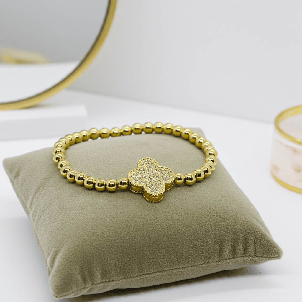 Gold slip on bracelet with a clover-shaped charm on a green pillow