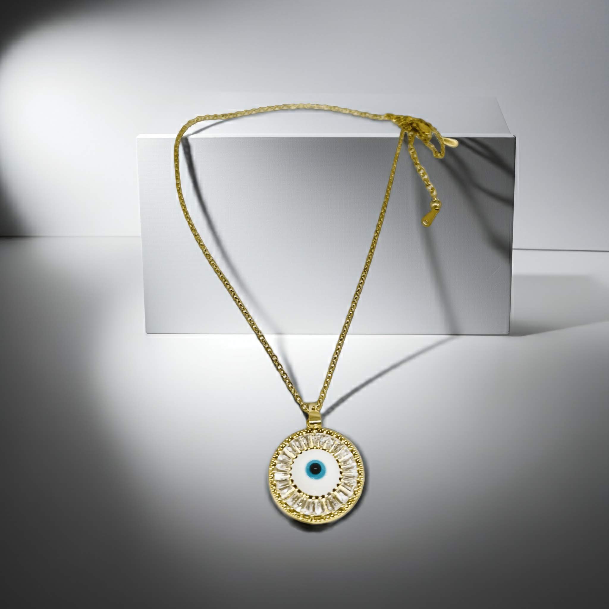 Gold necklace with a circular pendant featuring an eye design on a gray background