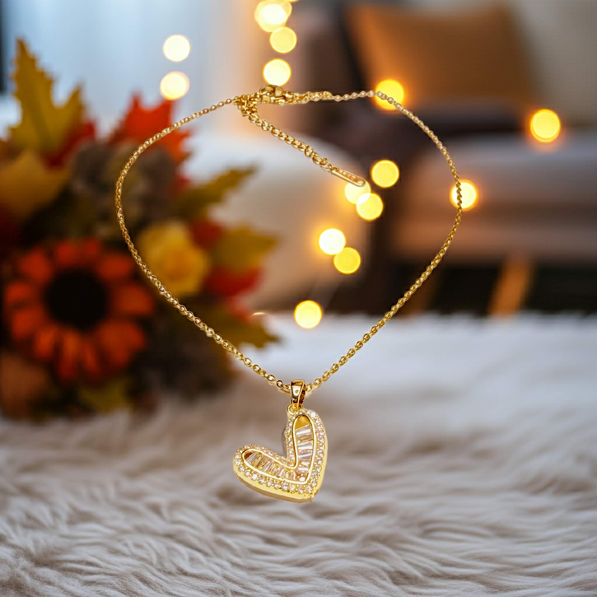 Gold-plated chain with a heart-shaped swarovski pendant on a soft surface with blurred lights and flowers in the background