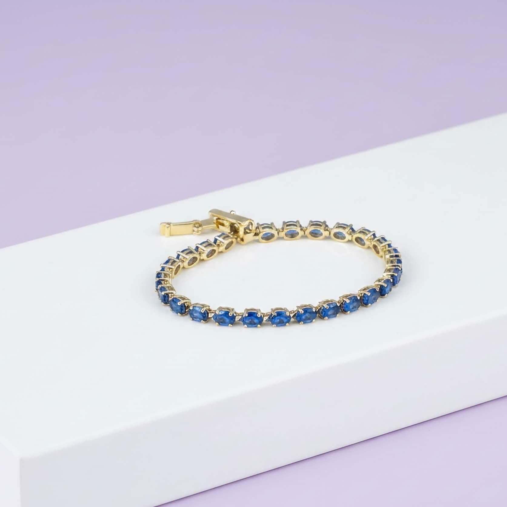 Luxury Statement Jewelry Bracelets collection Gold bracelet with blue stones on a white box against a light purple background