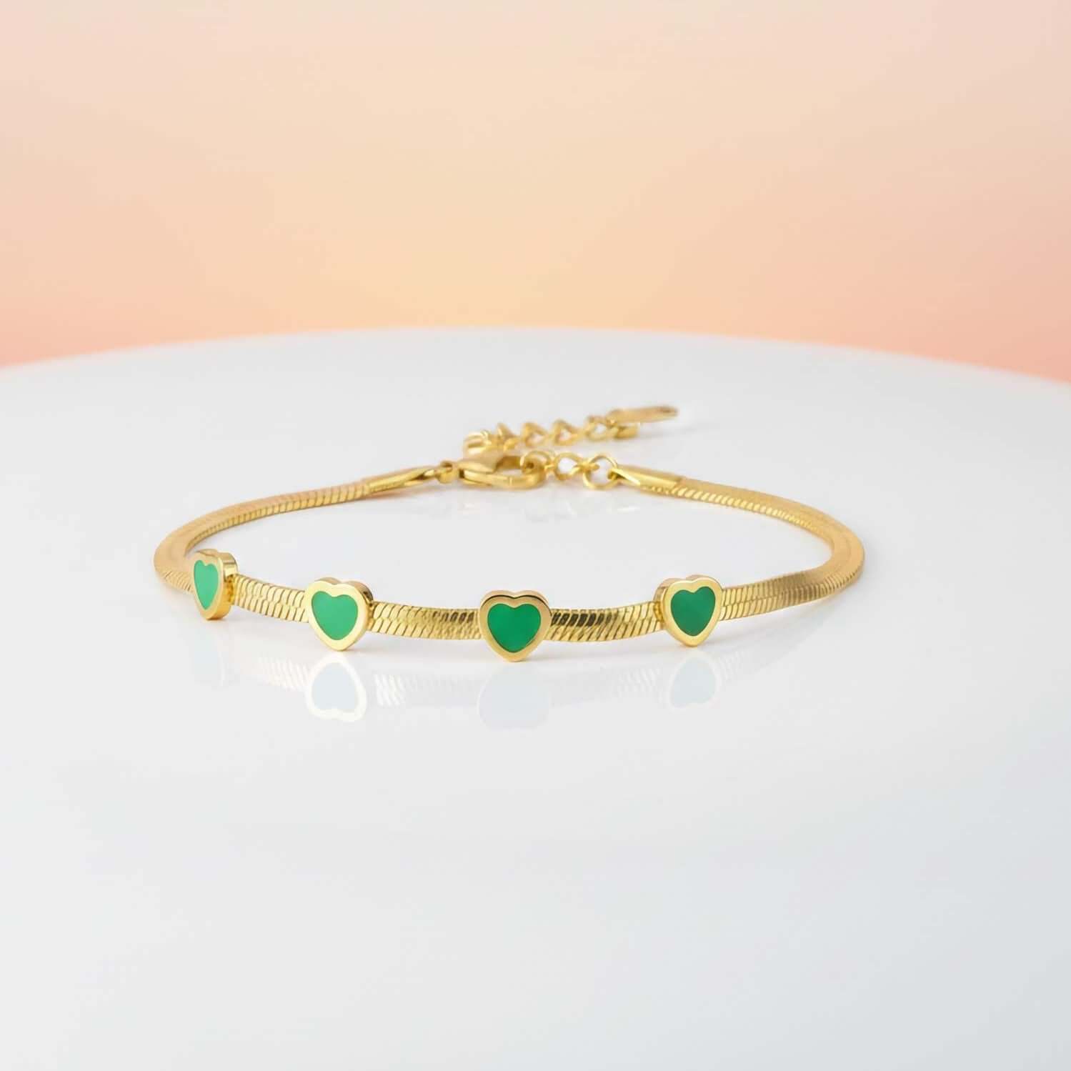 Elegant Green Crystal Bracelet  with green heart charms on a light gray surface with a pink gradient background