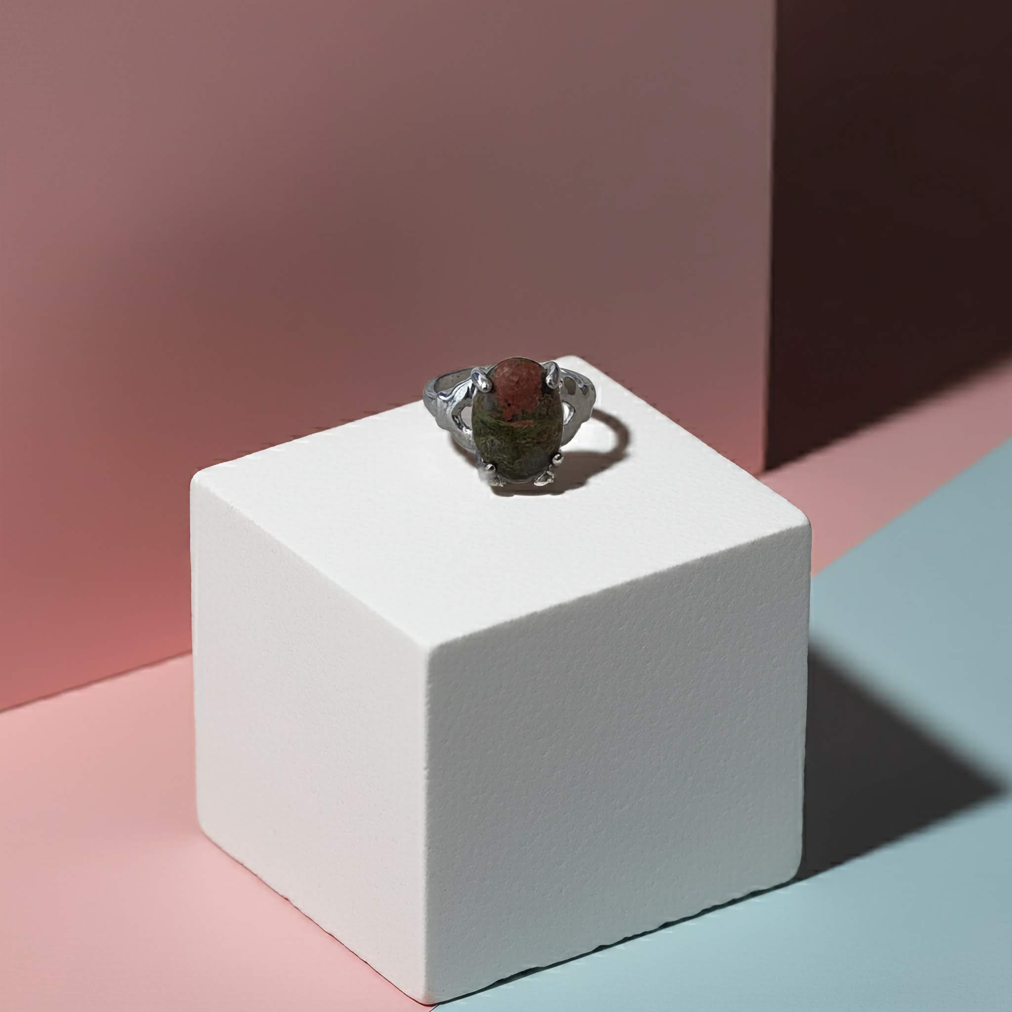 Ring with a green stone on a white cube against a pink and blue gradient background