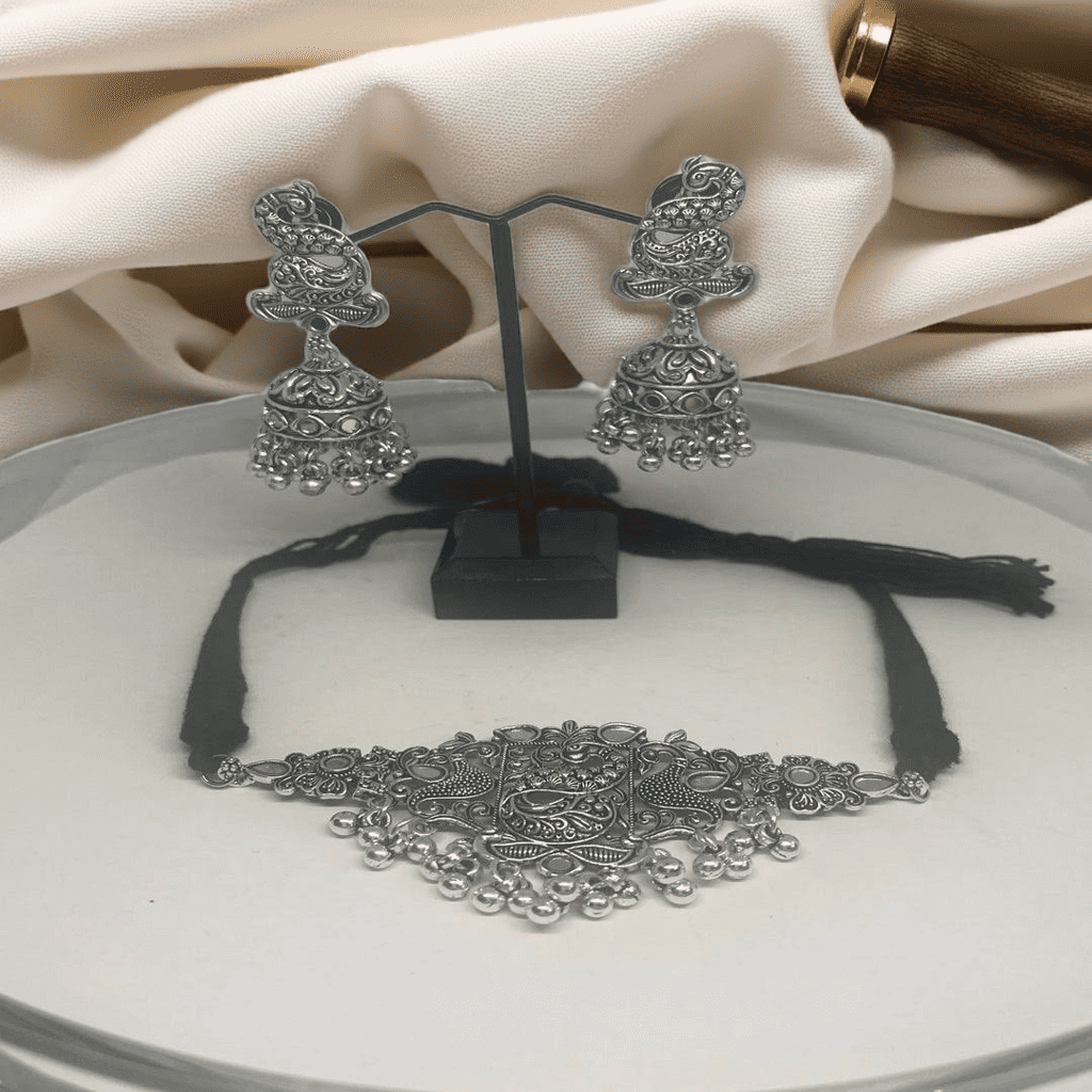 Oxidized silver necklace and earrings on a white plate with a beige fabric background