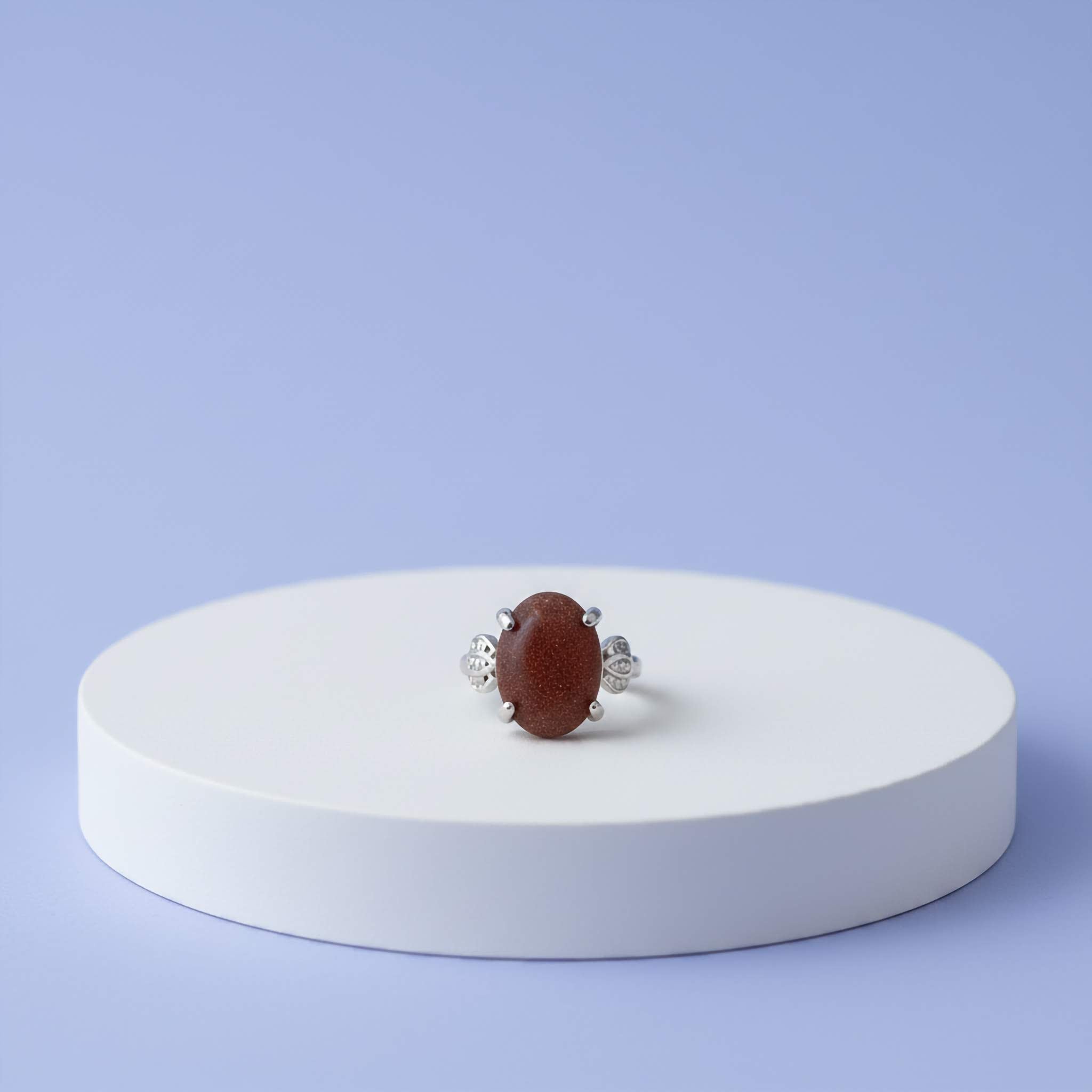 Ring with a brown sparkly stone on a white platform against a light blue background