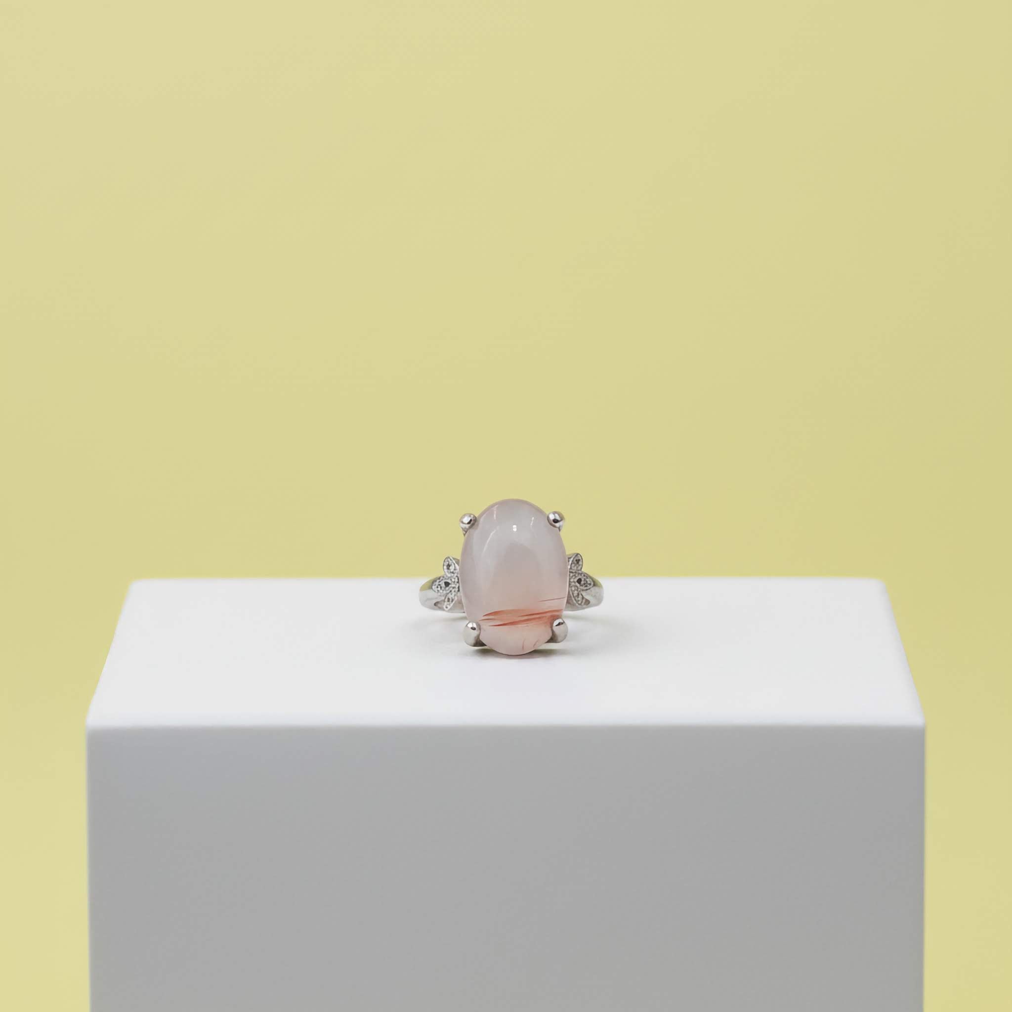 Silver ring with a pink stone on a white block against a yellow background