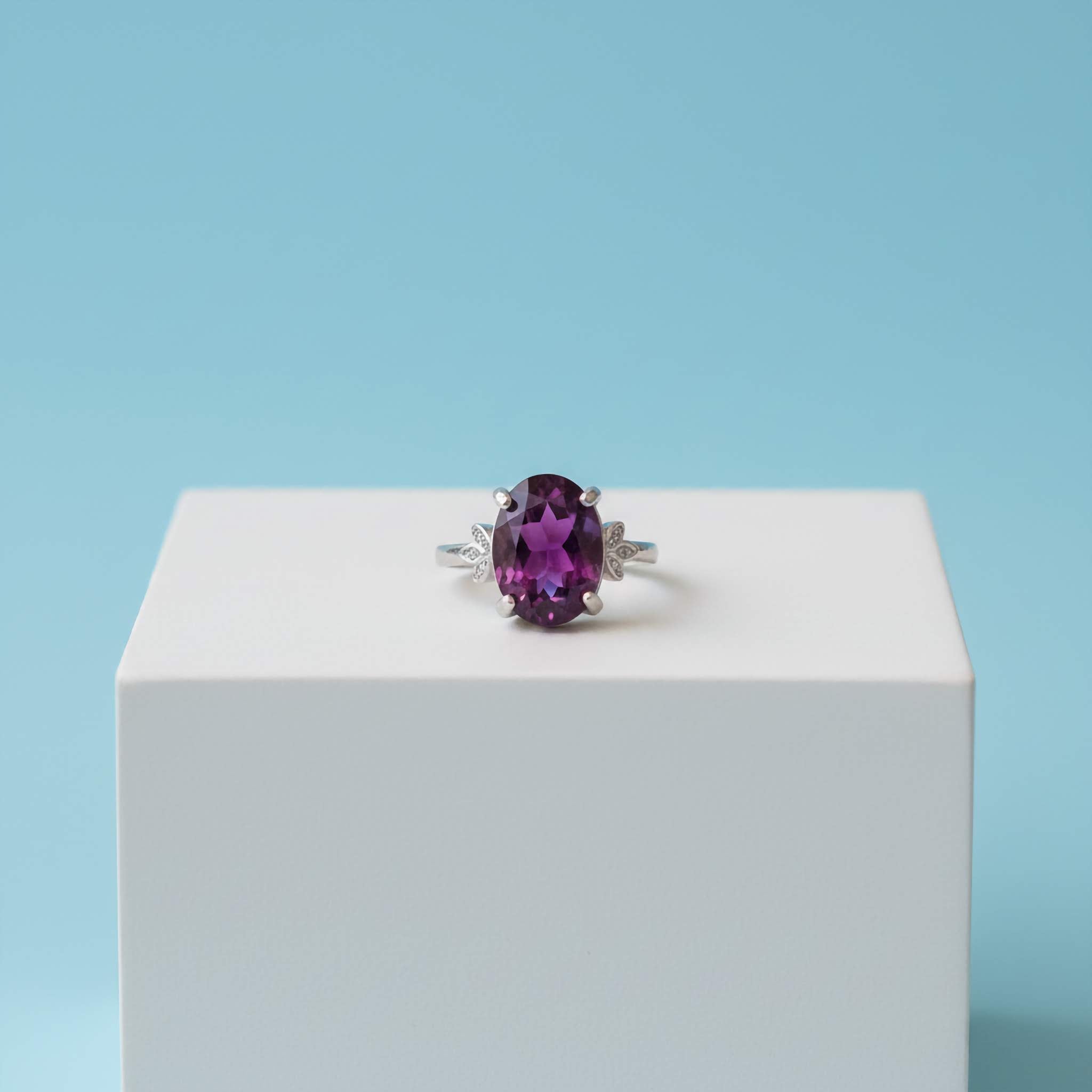 Ring with a purple gemstone on a white block against a light blue background