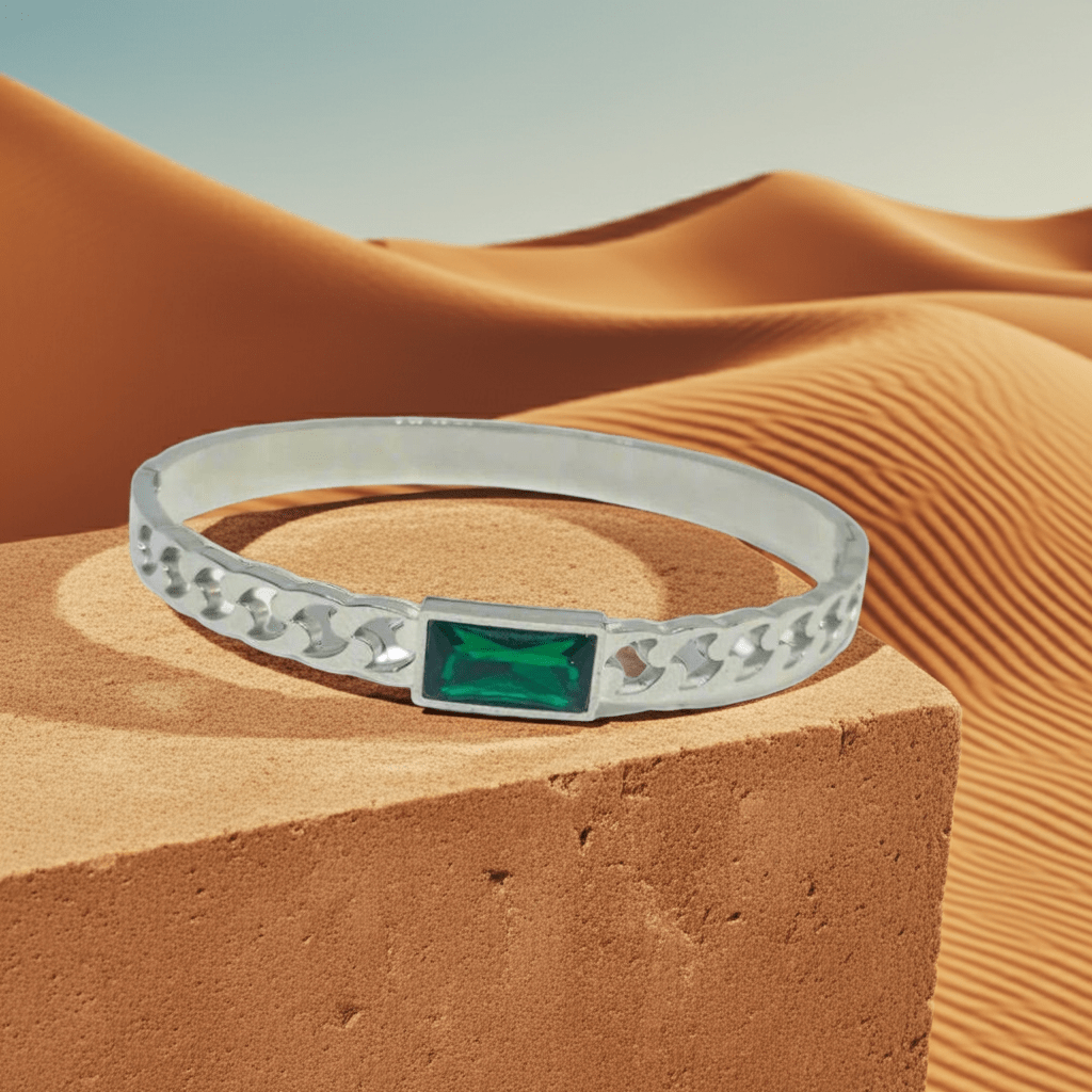Silver bracelet with a green gemstone on a desert sand background