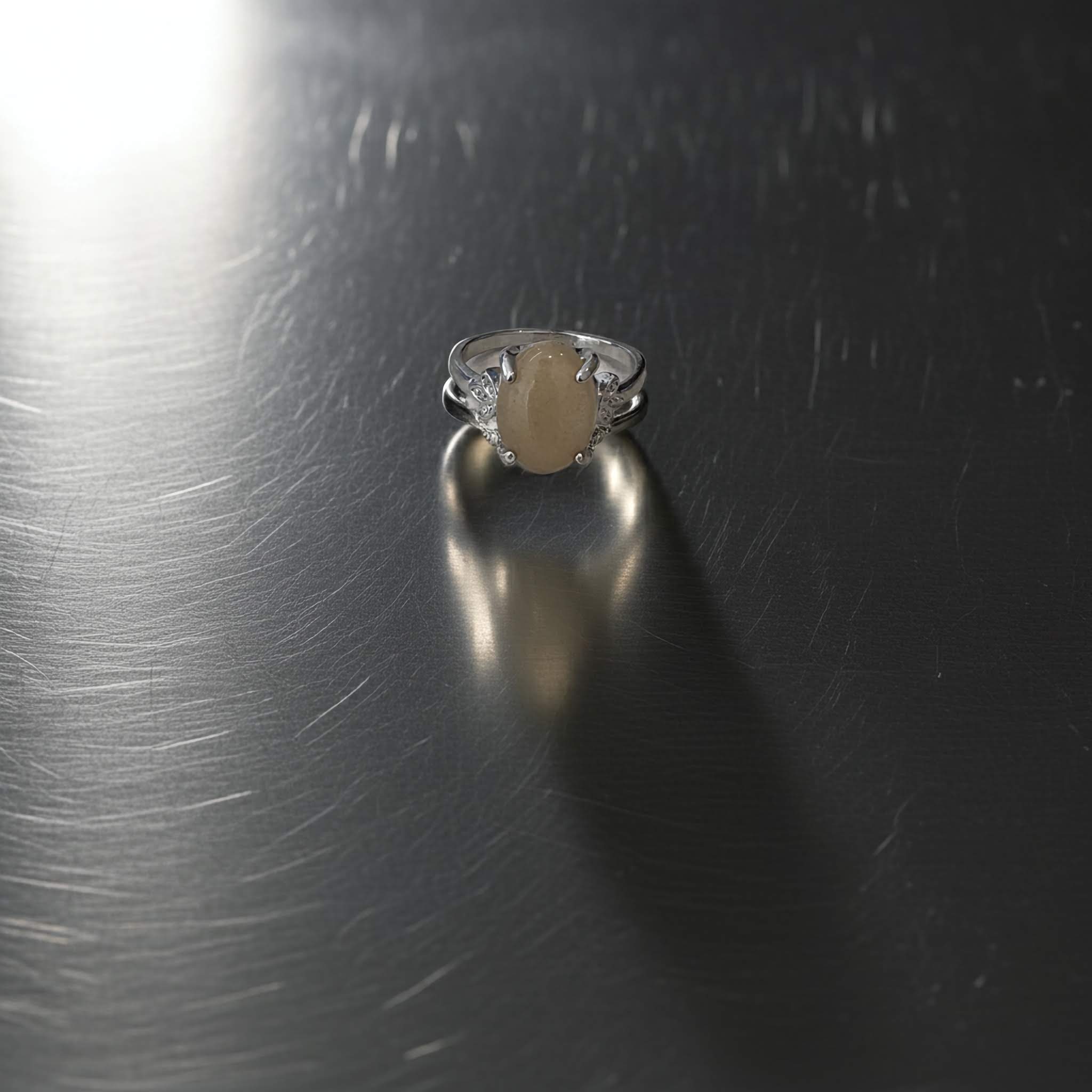 Silver ring with a beige stone on a metallic surface