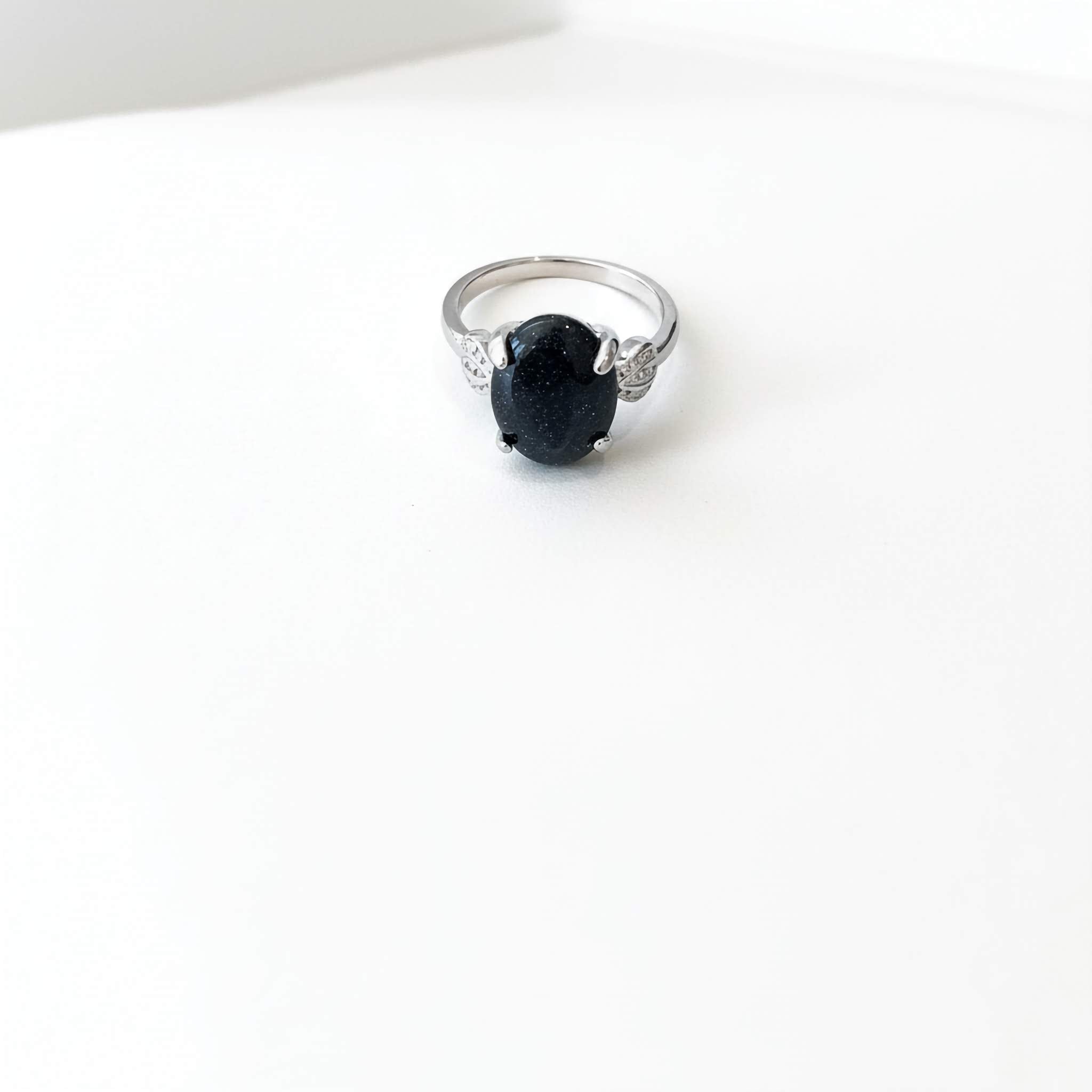 Silver ring with a dark blue sparkly gemstone on a white background