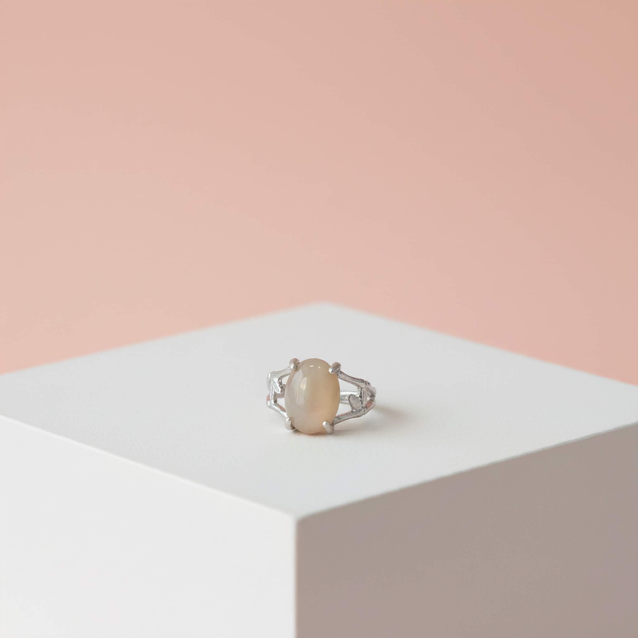 Silver ring with a large peach coloured stone on a white platform with a pink background