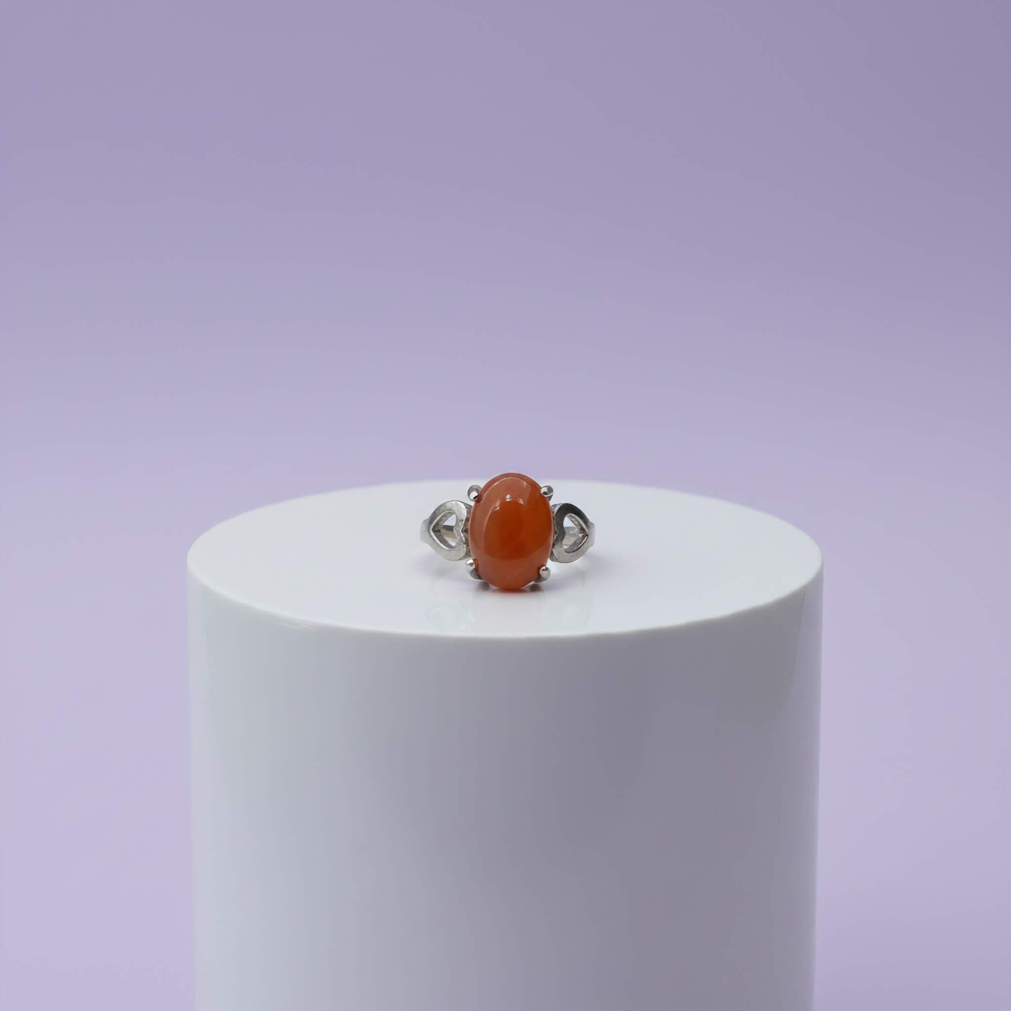 Silver ring with a maroon stone on a white cylindrical stand against a light purple background