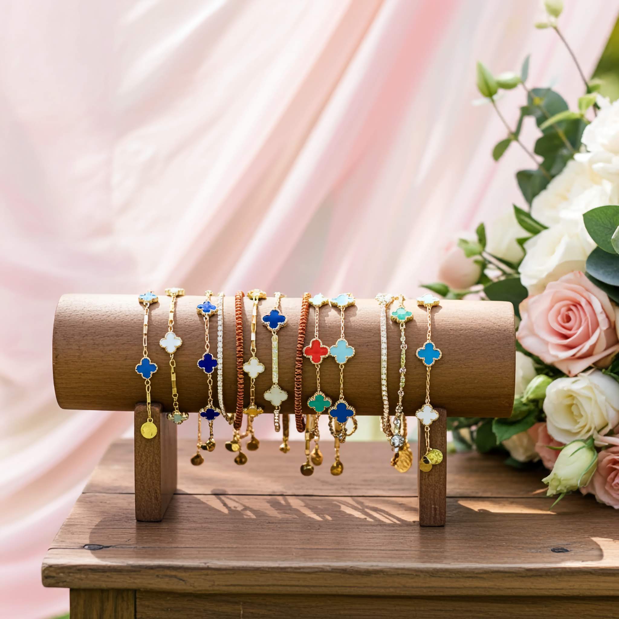 Set of multi color gold plated clover bracelets on a wooden stand, with flowers in the background.