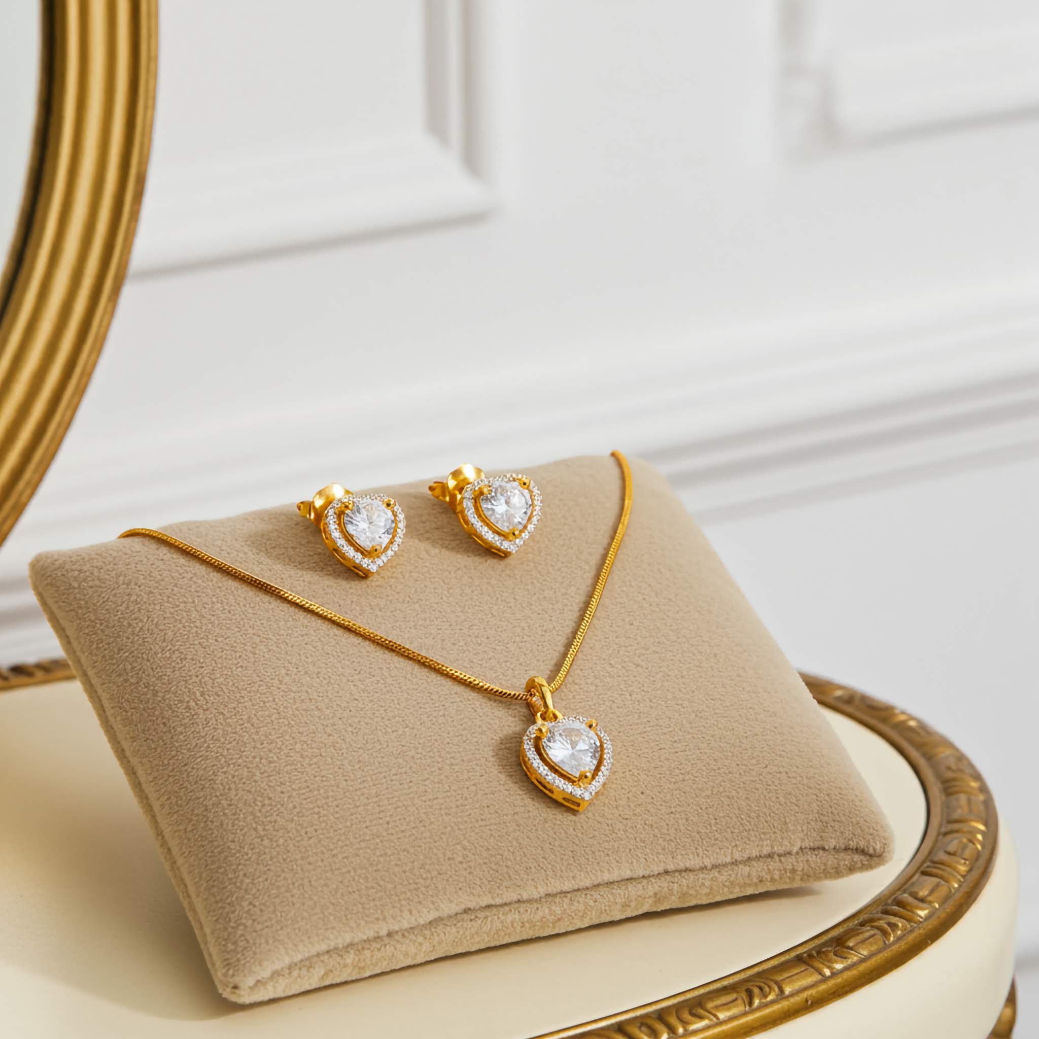 heart shaped zirconia diamond 18k Gold plated jewelry set of pendant and earrings on a beige cushion, placed on a decorative stand.
