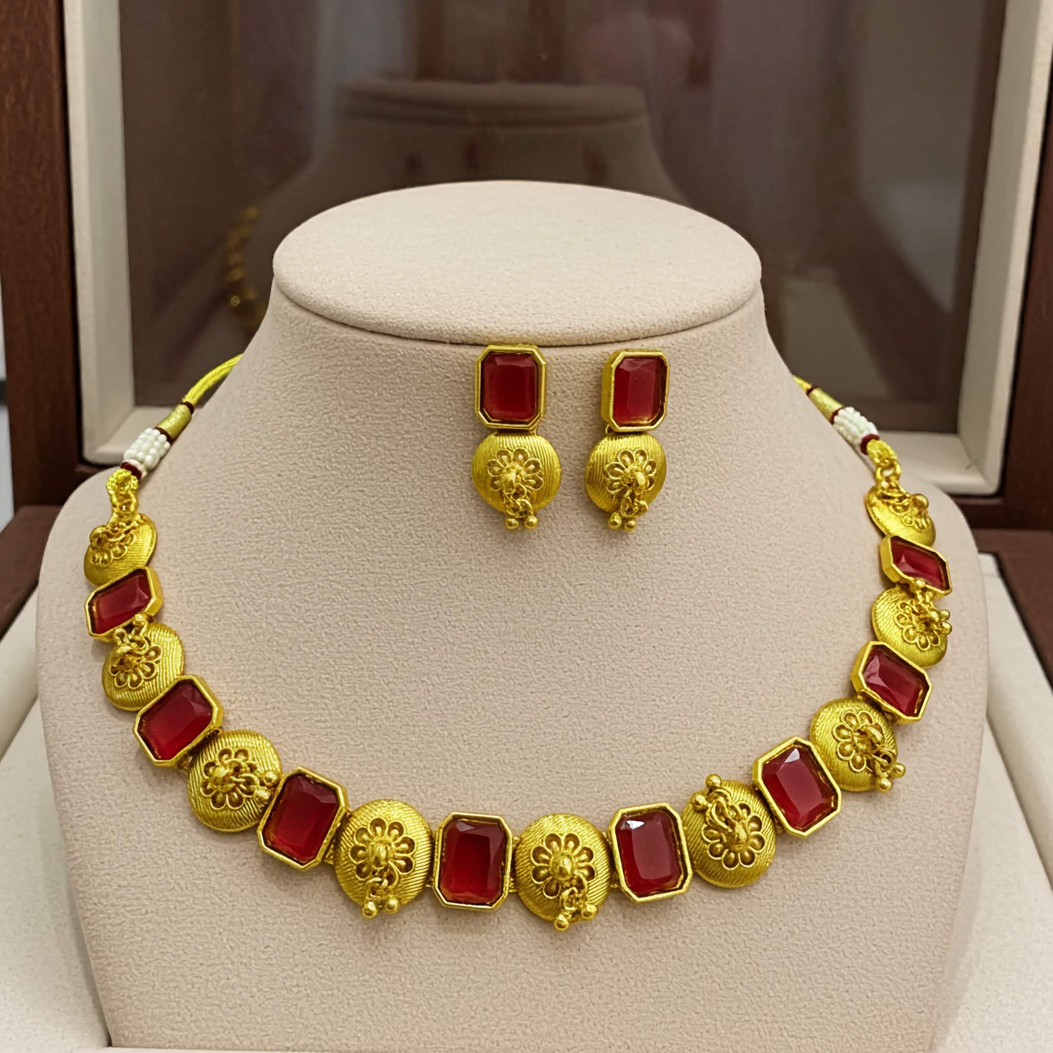 Gold necklace with red stones and matching earrings on a mannequin bust.