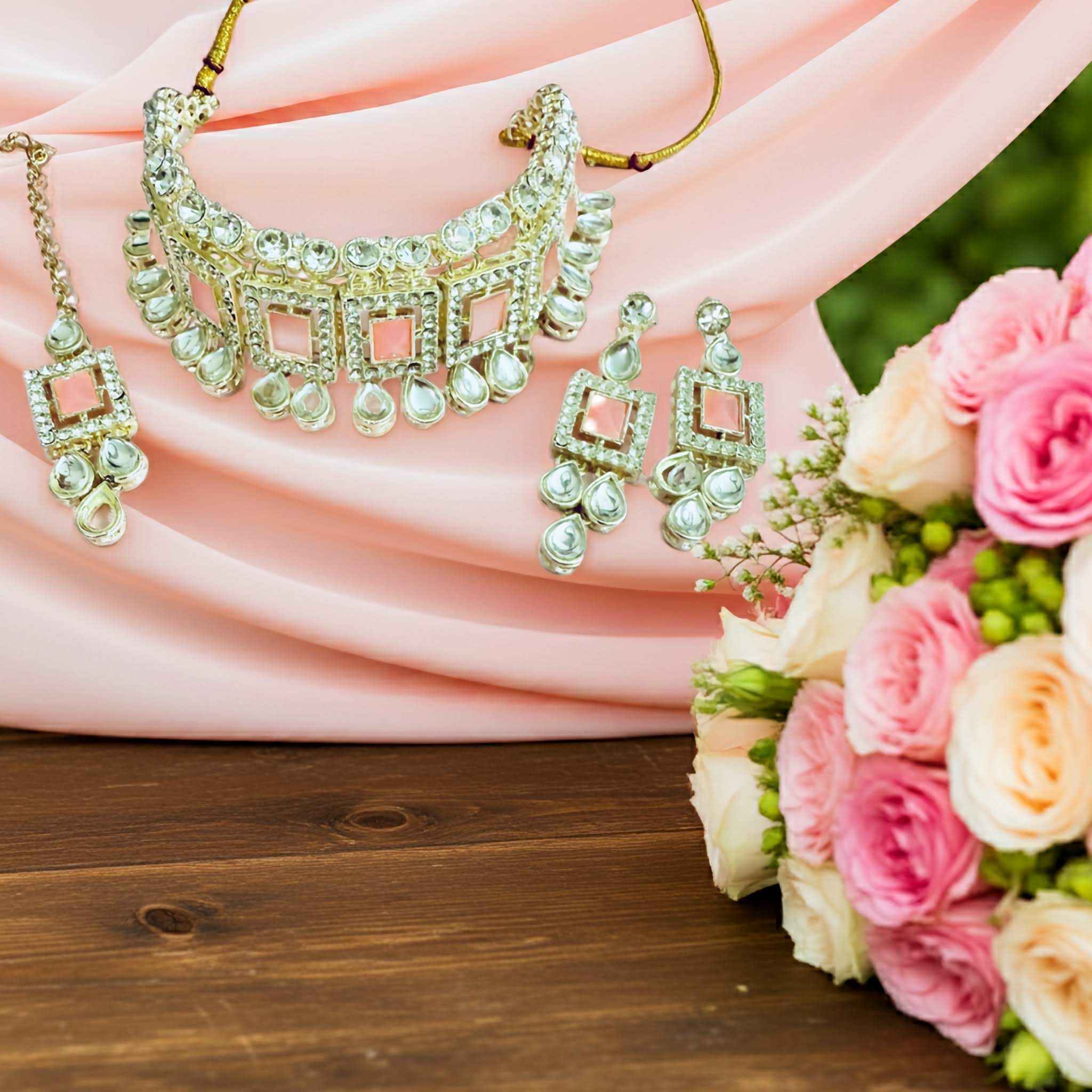 Silver choker necklace, earrings and tikka  with pink stones on it with pink roses on a wooden surface