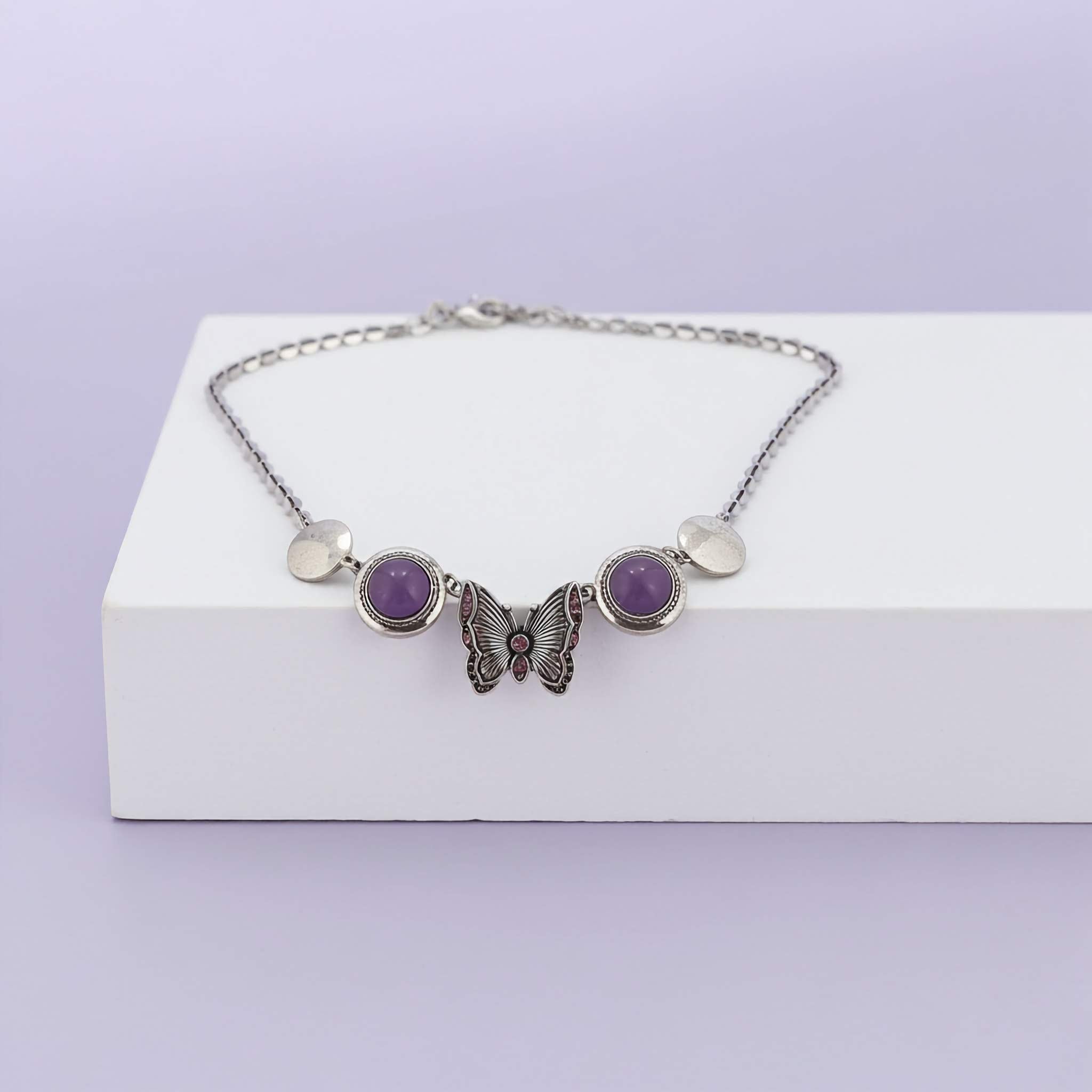 A Butterfly necklace with purple stones on a white box against a light purple background